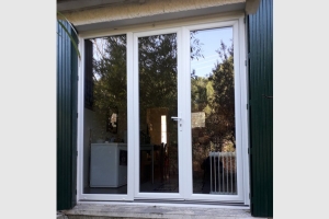 Porte-fenêtre en pvc blanc 3 vantaux dont un fixe. Vitrage jusqu'en bas de la porte.